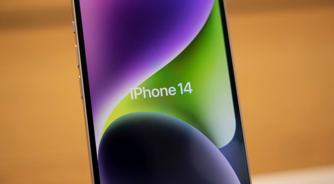 iPhone 14 in einem Apple Store vor orangefarbenem Hintegrund