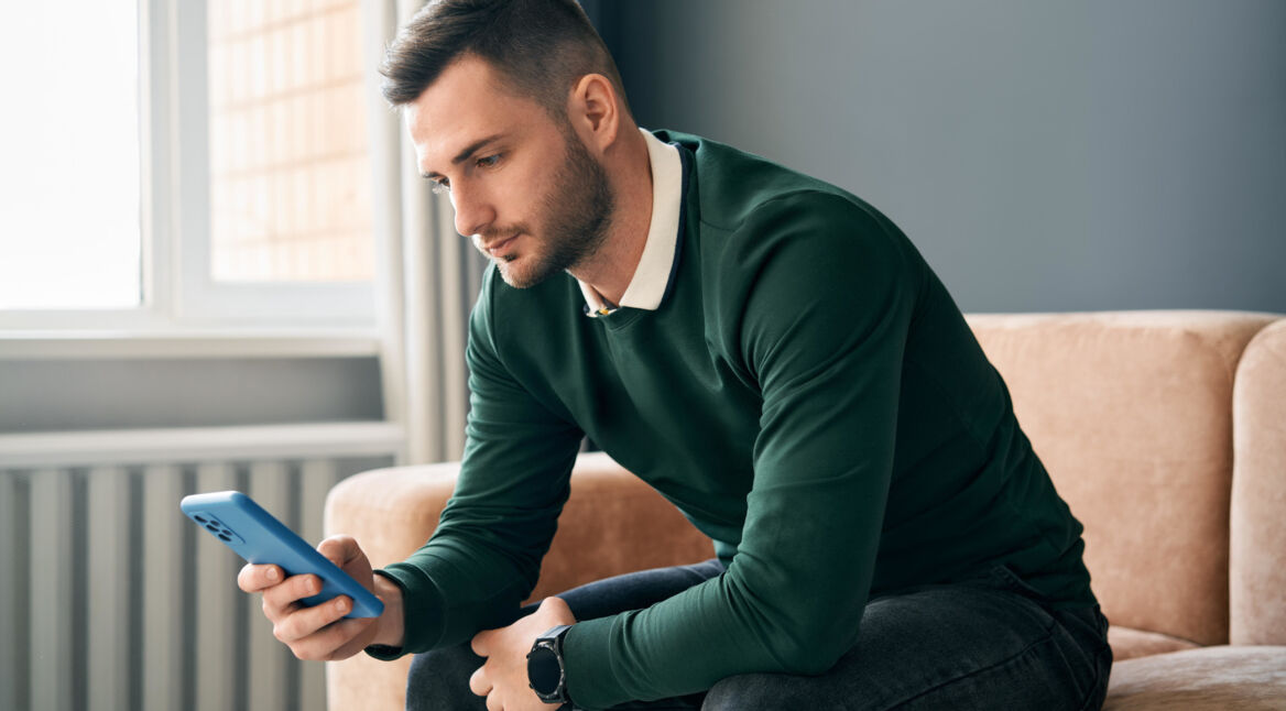 Junger Man auf Ledersofa guckt auf sein Smartphone