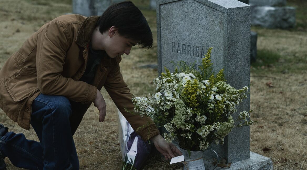 Ein junger Mann kniet an einem Grab