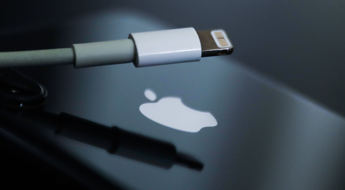 Lightning-Kabel vor schwarzem iPhone mit weißem Apple-Logo auf der Rückseite