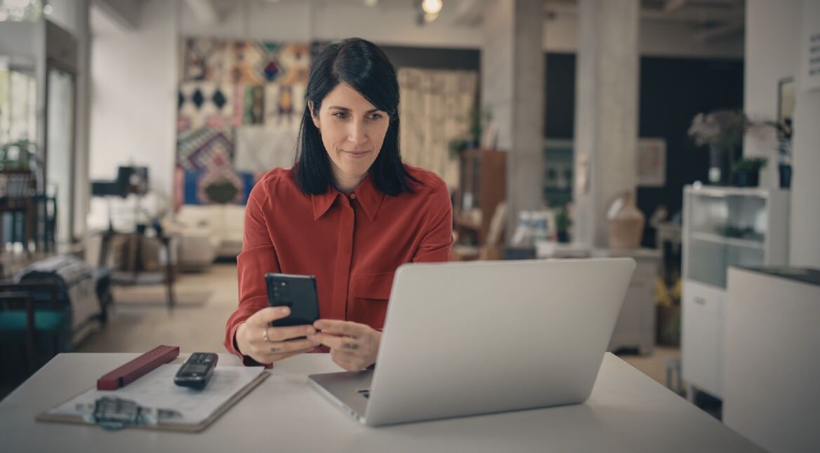 Frau mit Smartphone vor Laptop