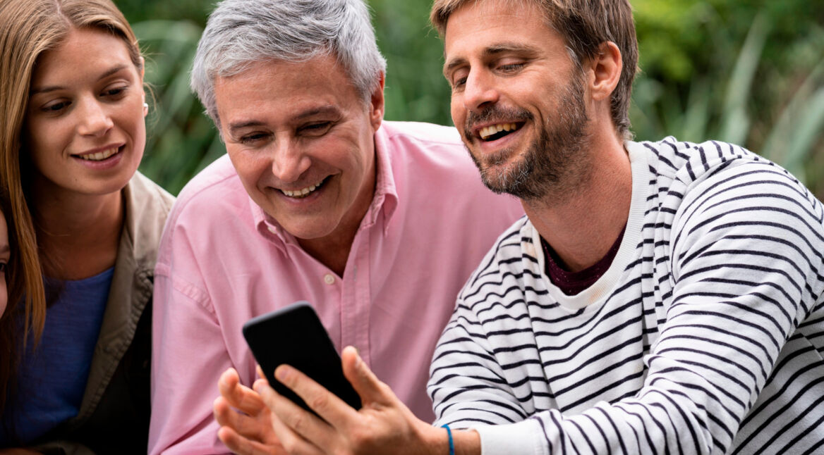 Junger Mann zeigt einem älteren Herren und einer jungen Frau etwas auf seinem Smartphone