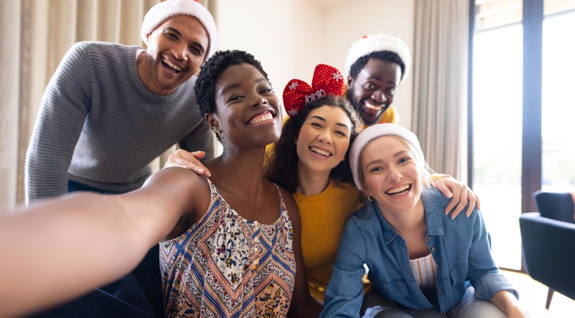 Gruppe junger Erwachsener im Wohnzimmer macht Selfie mit Weihnachts-Mützen