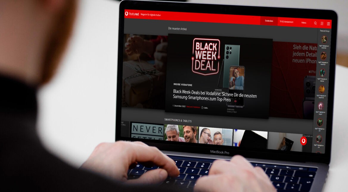 Mann sitzt vor MacBook Pro und hat die Finger auf der Tastatur, im Display ist die featured-Homepage zu sehen.