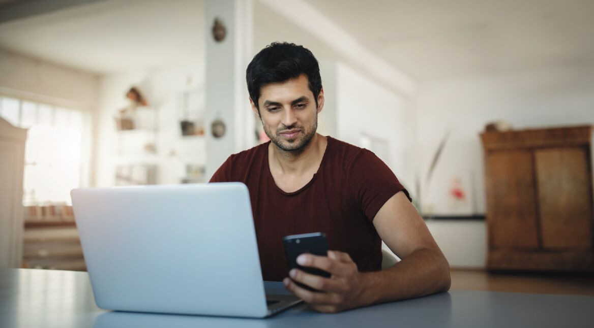 Mann mit Smartphone vor Laptop