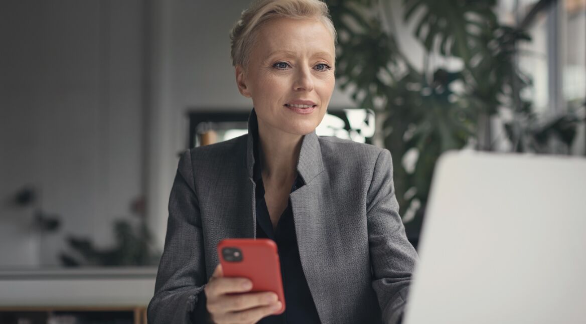 Frau mit Smartphone vor Laptop