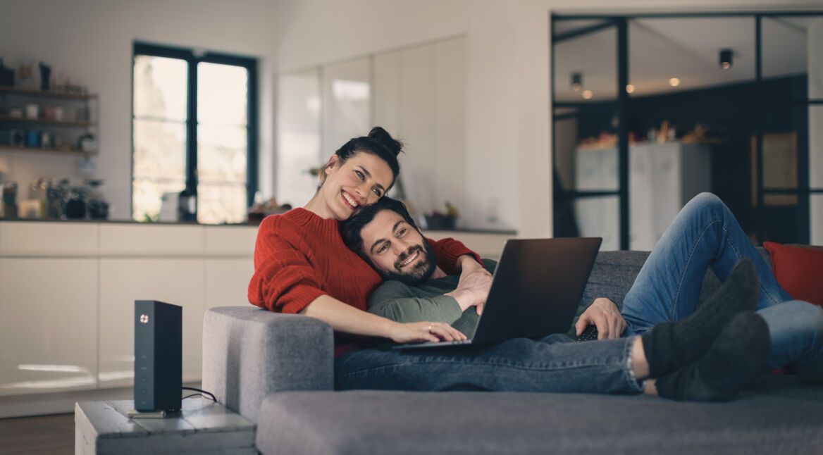 Ein Paar sitzt gemütlich auf der Couch mit einem Laptop auf dem Schoß