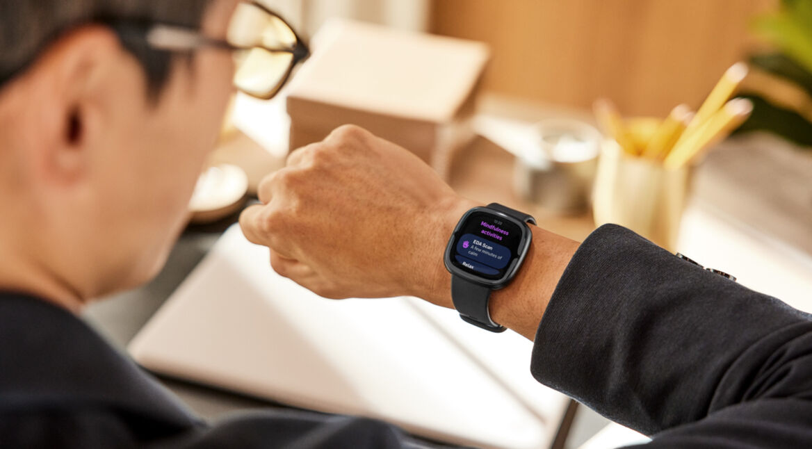 Blick über Schulter von Geschäftsmann im Anzug auf Smartwatch Fitbit Sense 2