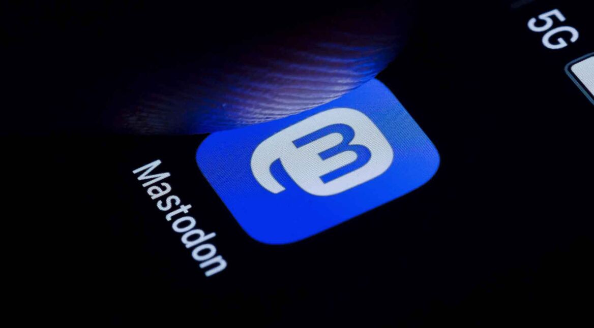 Das App-Logo von Mastodon auf einem Smartphone-Bildschirm, ein Stück über dem Bildschirm befindet sich ein Finger in der Luft