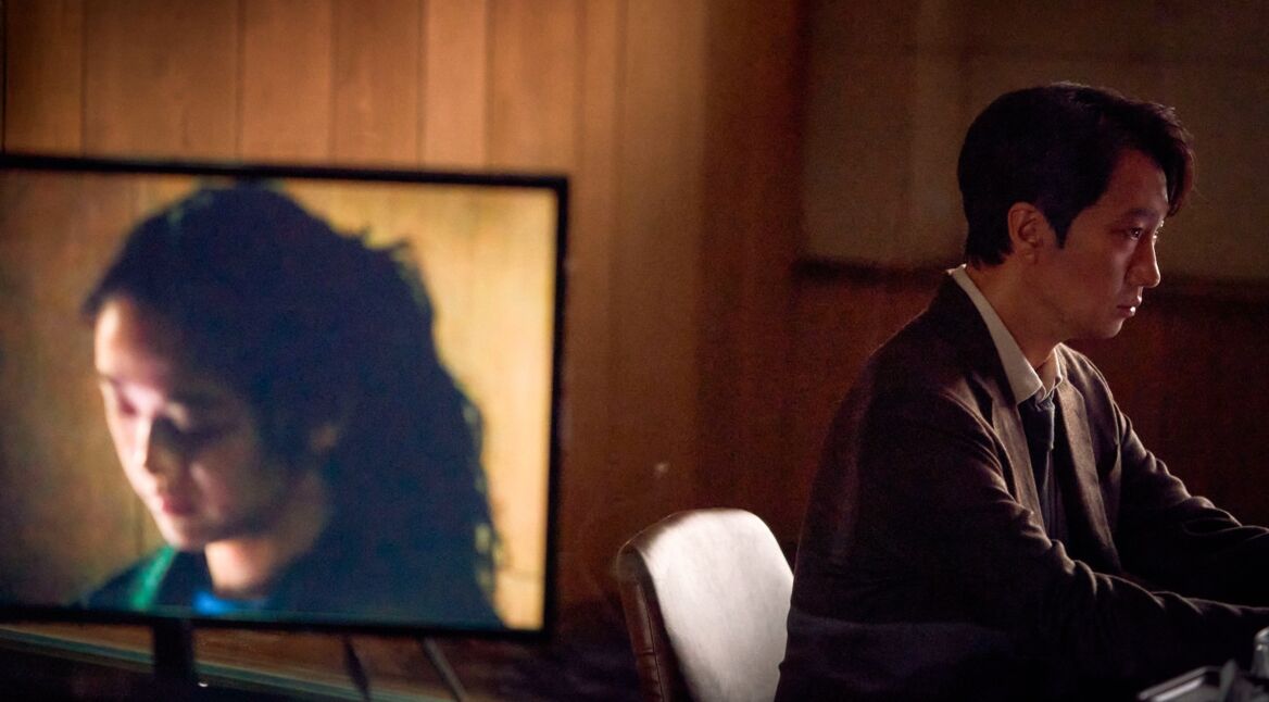 Eine FRau auf dem Monitor, ein Mann am Schreibtisch