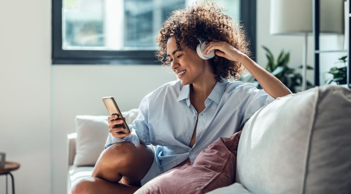 Junge Frau mit Kopfhörer und Smartphone auf dem Sofa