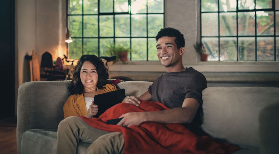Mann und Frau sitzen gemeinsam auf dem Sofa und schauen Fernsehen