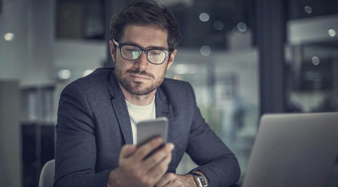 Mann mit Smartphone vor Laptop