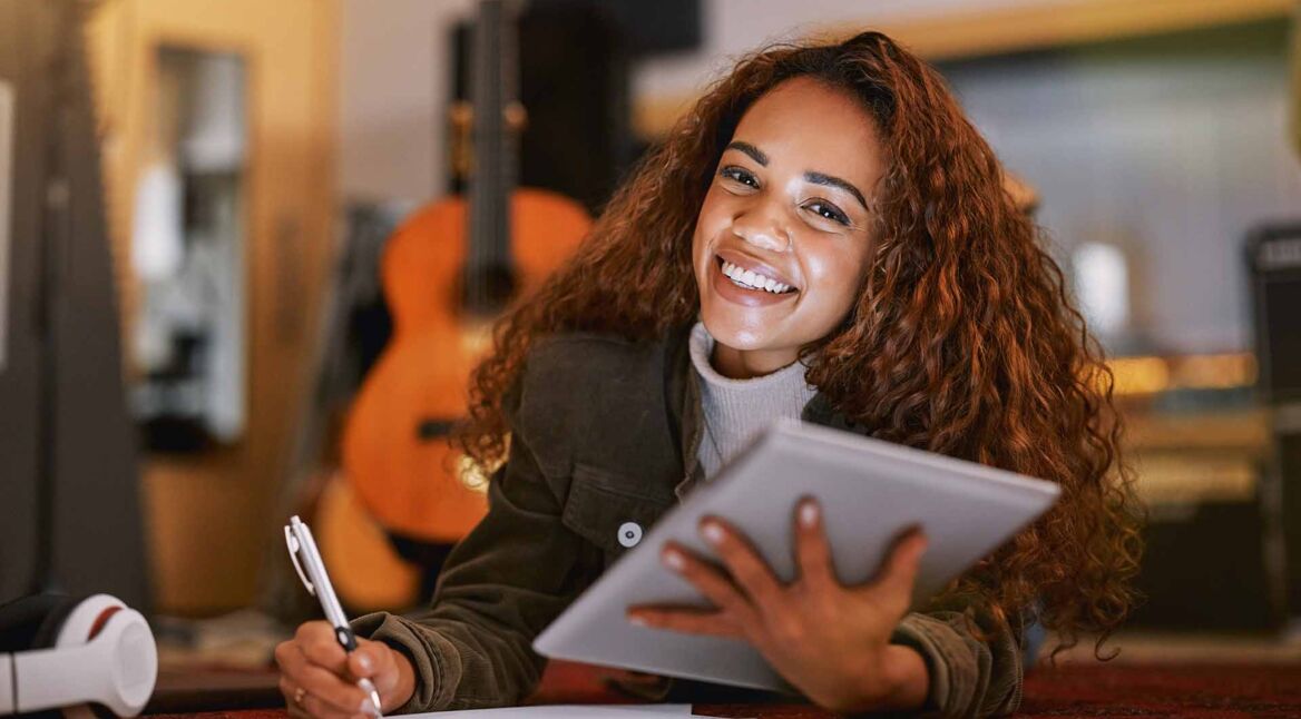 Eine Frau hält ein iPad in der Hand und macht sich Notizen auf einem Block