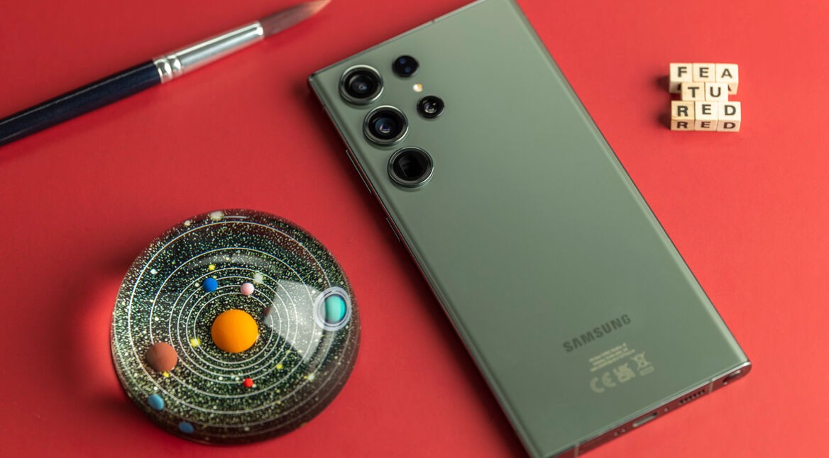 Rückseite des Smartphones Galaxy S23 Ultra neben einer buten Glaskugel auf rotem Untergrund