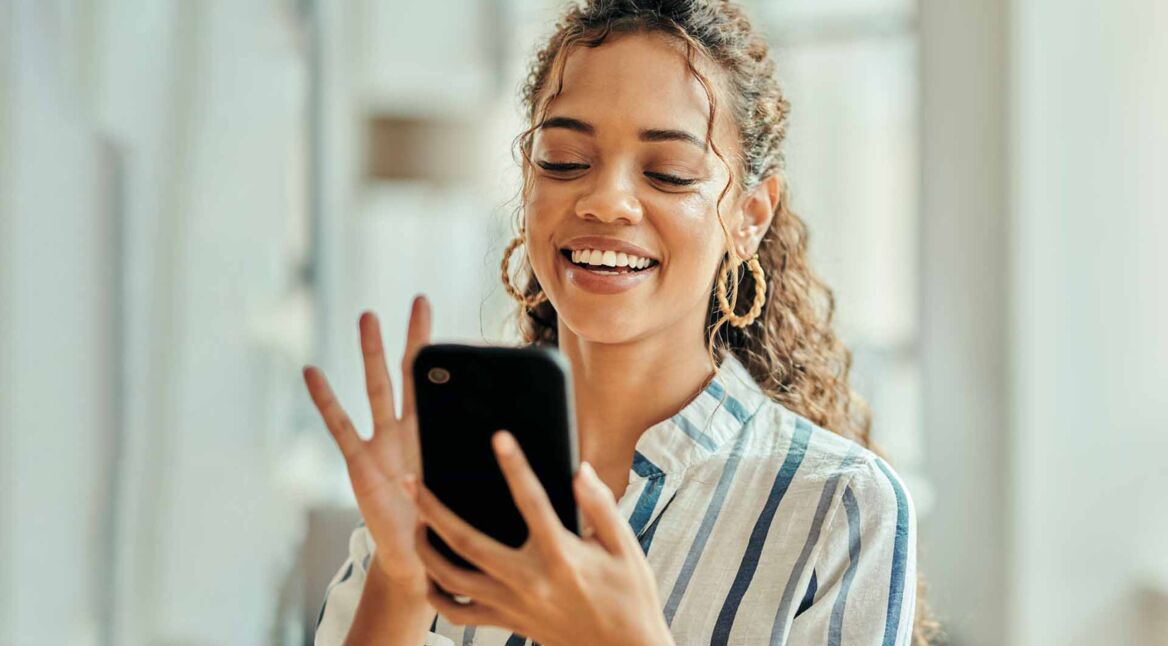 Eine Frau hält ein Handy in der Hand und lächelt.