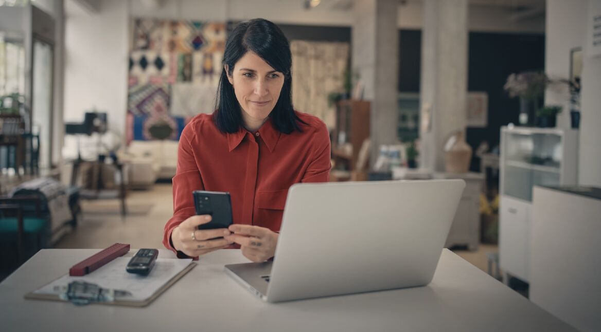 Frau mit Smartphone vor Laptop