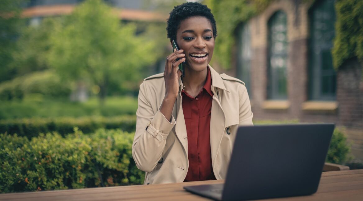 Frau am Handy vor Laptop