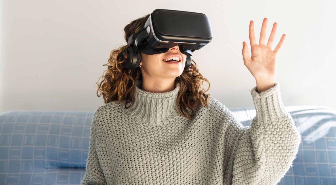 Eine Frau trägt eine VR-Brille und sitzt auf einem Sofa