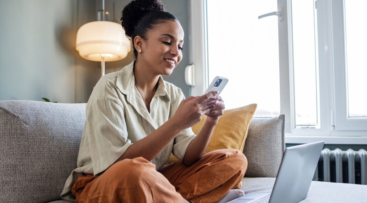 Frau sitzt auf dem Sofa und unternimmt Einstellungen zur Datensicherung an ihrem Smartphone