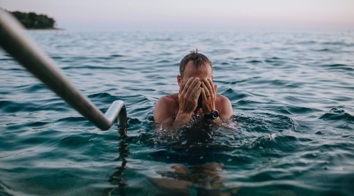 Mann am Strand bei Sonnenuntergang beim Schwimmen im blauen Ozean