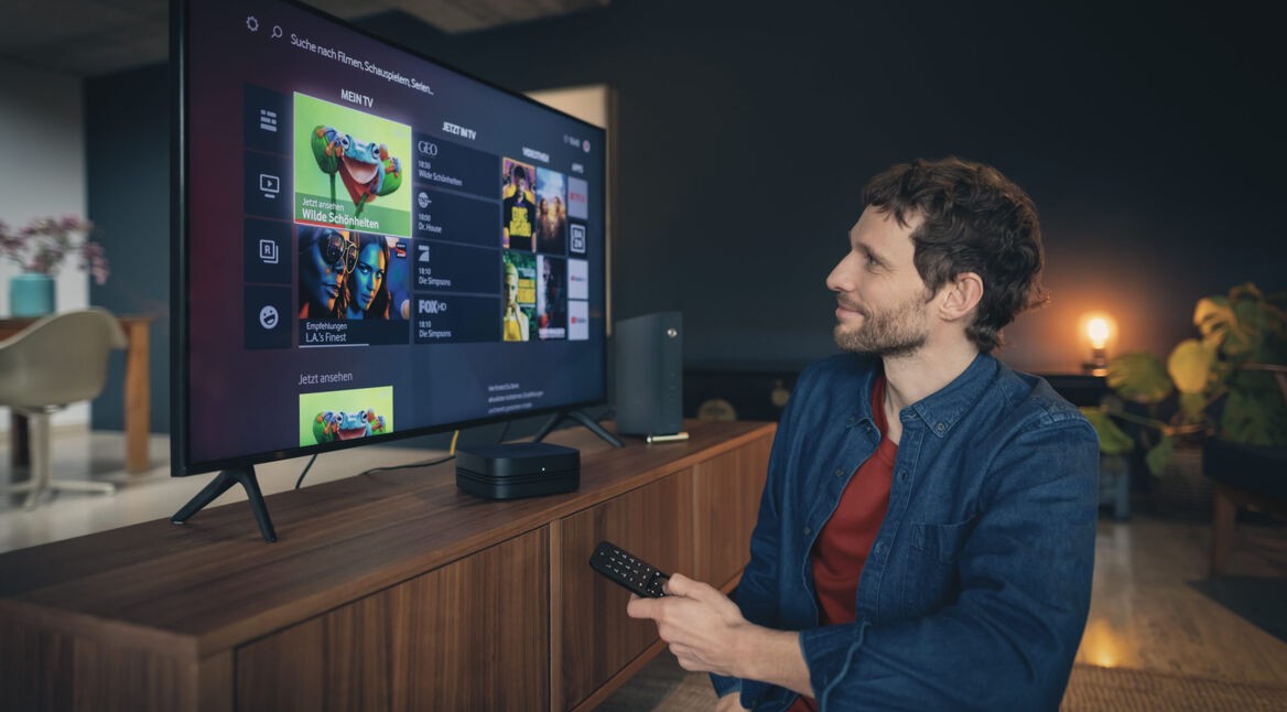 Mann sitzt mit Fernbedienung vor GigaTV von Vodafone