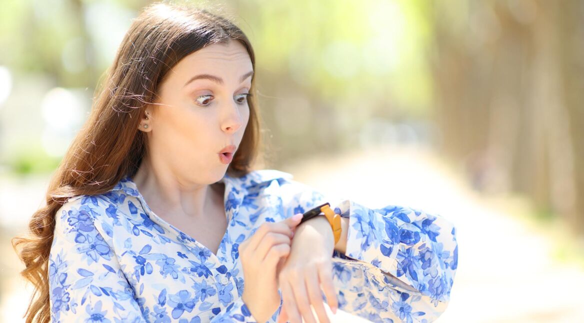 Überraschte Frau, die ihre Smartwatch in einem Park überprüft