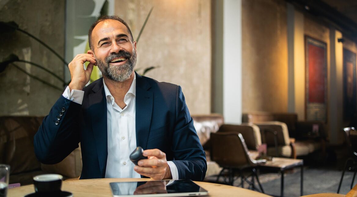 Ein lächelnder Mann in einem Café setzt sich In-Ear-Kopfhörer ein.