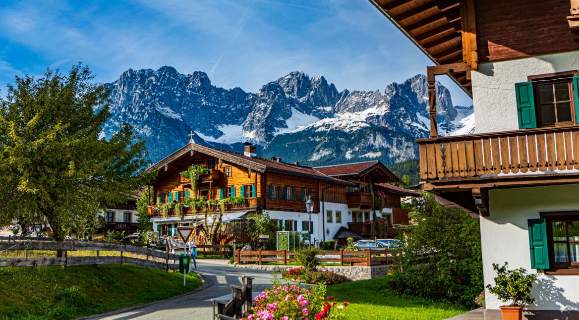 Ein Bergdorf mit Holzhäusern vor Alpenpanorama