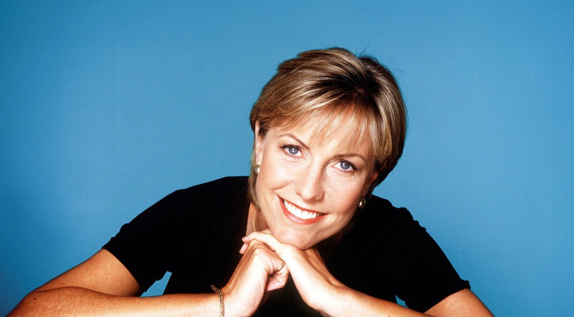 Jill Dando, eine Frau mit kurzen blonden Haaren, legt den Kopf auf die Hände und lächelt in die Kamera.