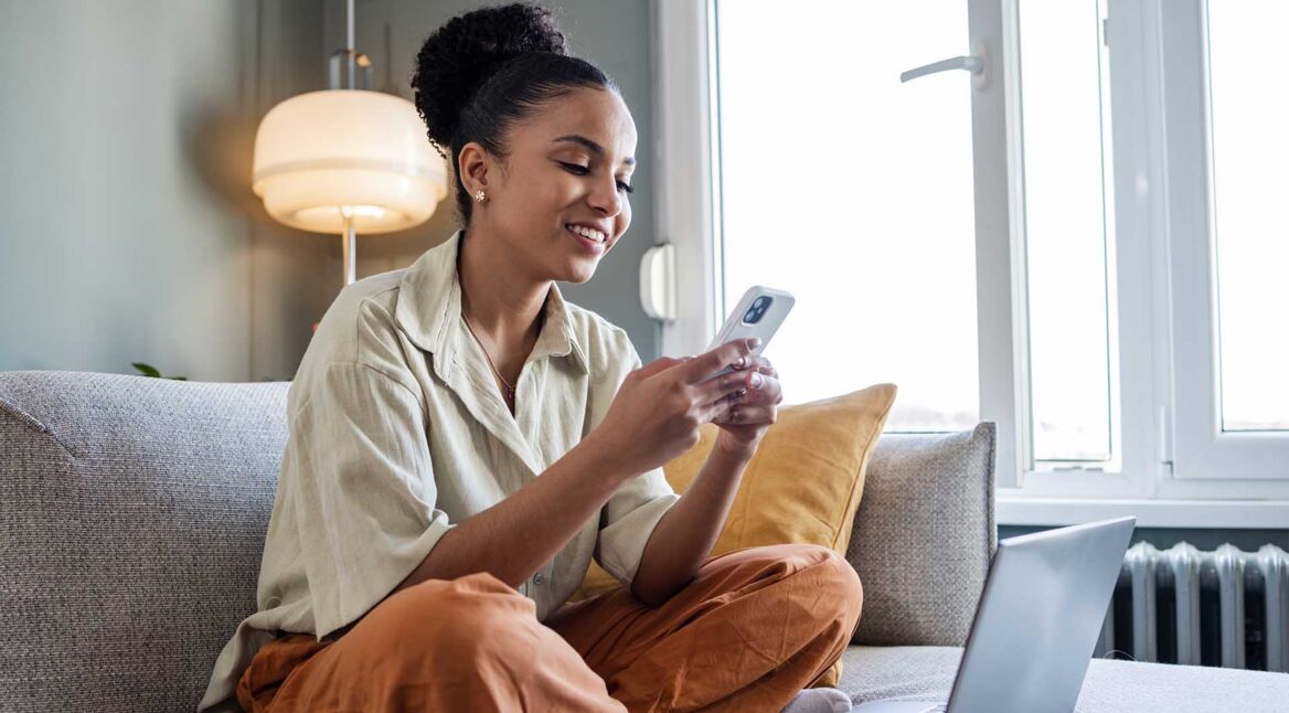 Eine junge Frau sitzt mit ihrem Smartphone in den Händen auf der Couch