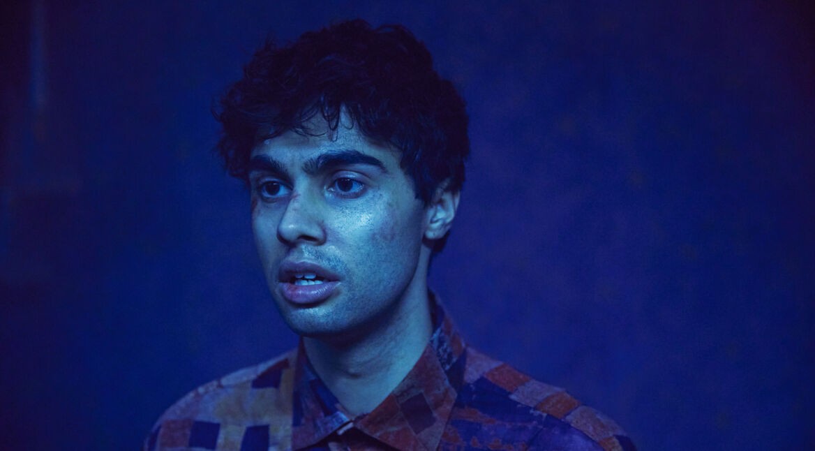 Tore: Ein Mann schaut verloren und geplagt links an der Kamera vorbei, vor einem dunkelblauen Hintergrund.