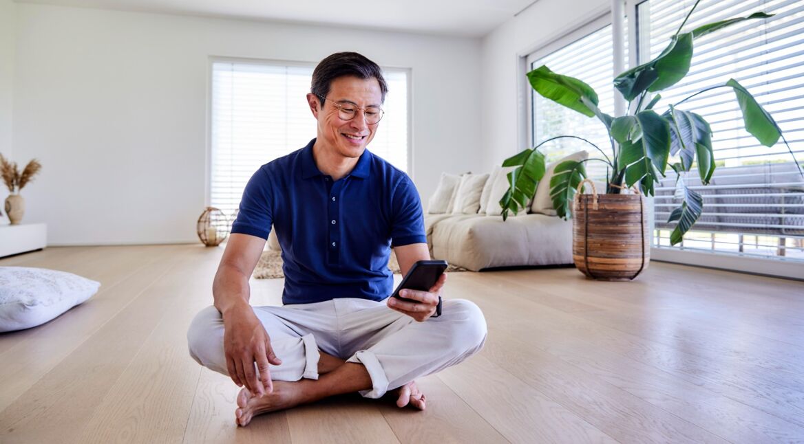 Mann mit Smartphone hockt auf dem Fußboden