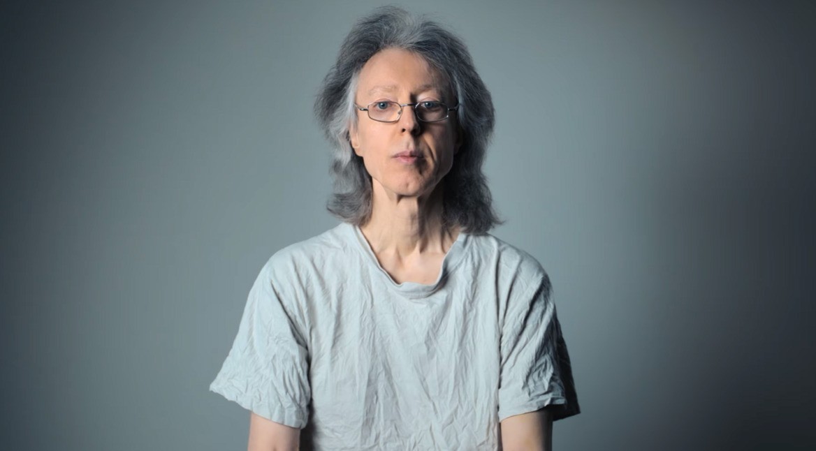 Cyberbunker bei Netflix: Ein älterer Mann mit schulterlangem grauem Haar, einer Brille und grauem T-Shirt blickt frontal in die Kamera.