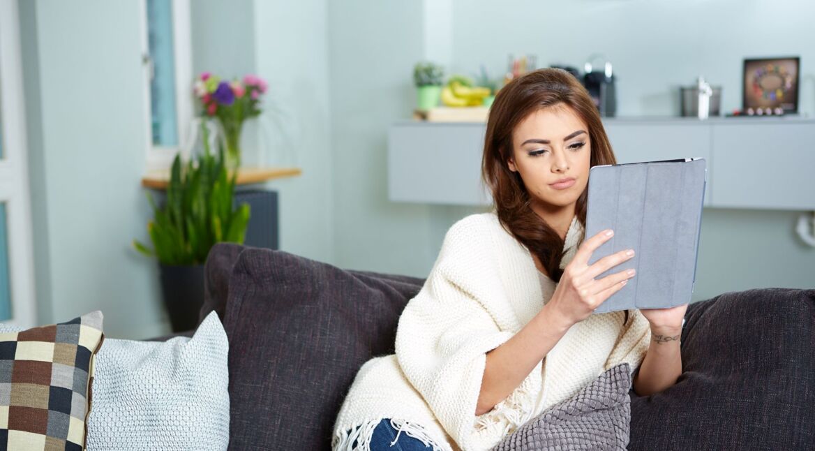 Frau sitzt auf Sofa und guckt auf ein Samsung-Tablet