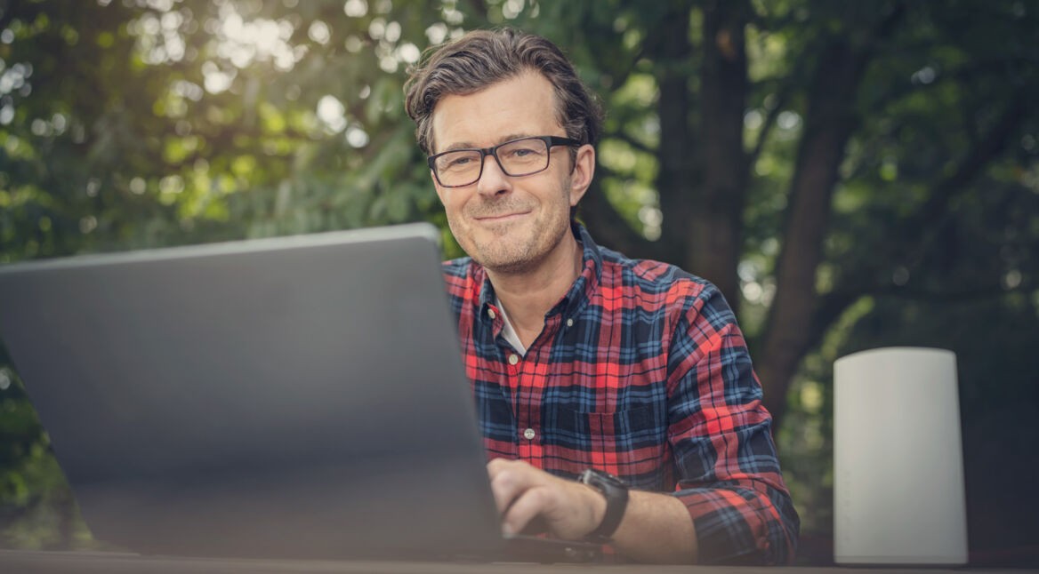 Ein Mann surft mit seinem Laptop, während er unter einem Baum sitzt