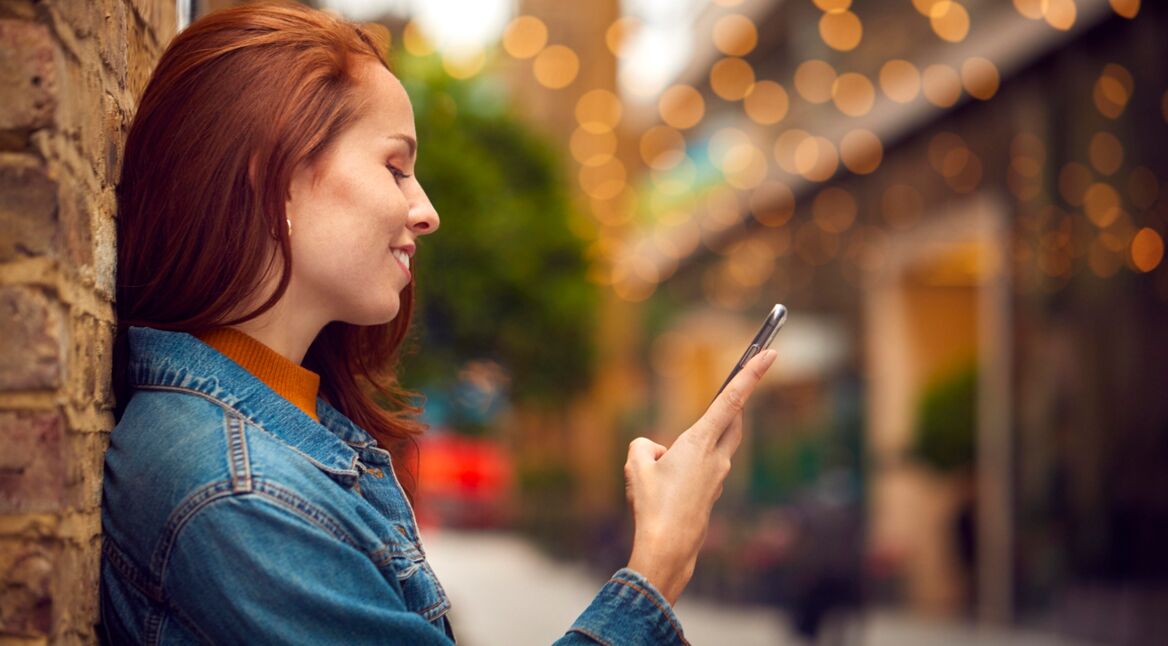 Eine junge Frau schaut auf ihr Handy und lächelt dabei.
