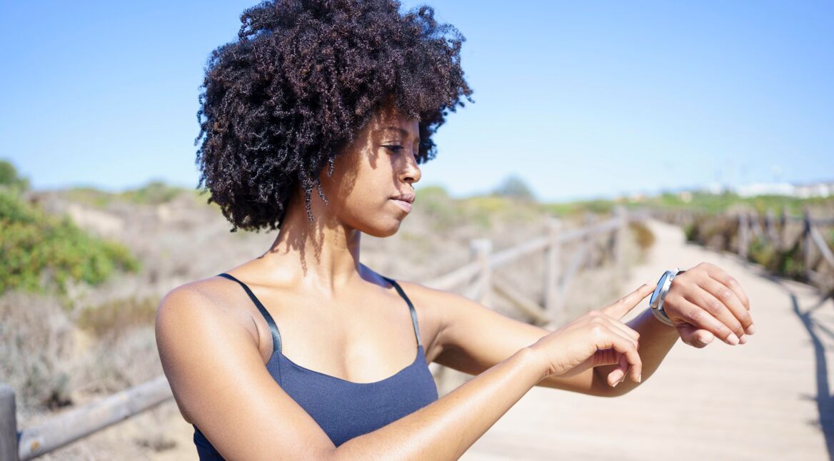 Junge Frau im Freien guckt auf ihre Smartwatch am Handgelenk