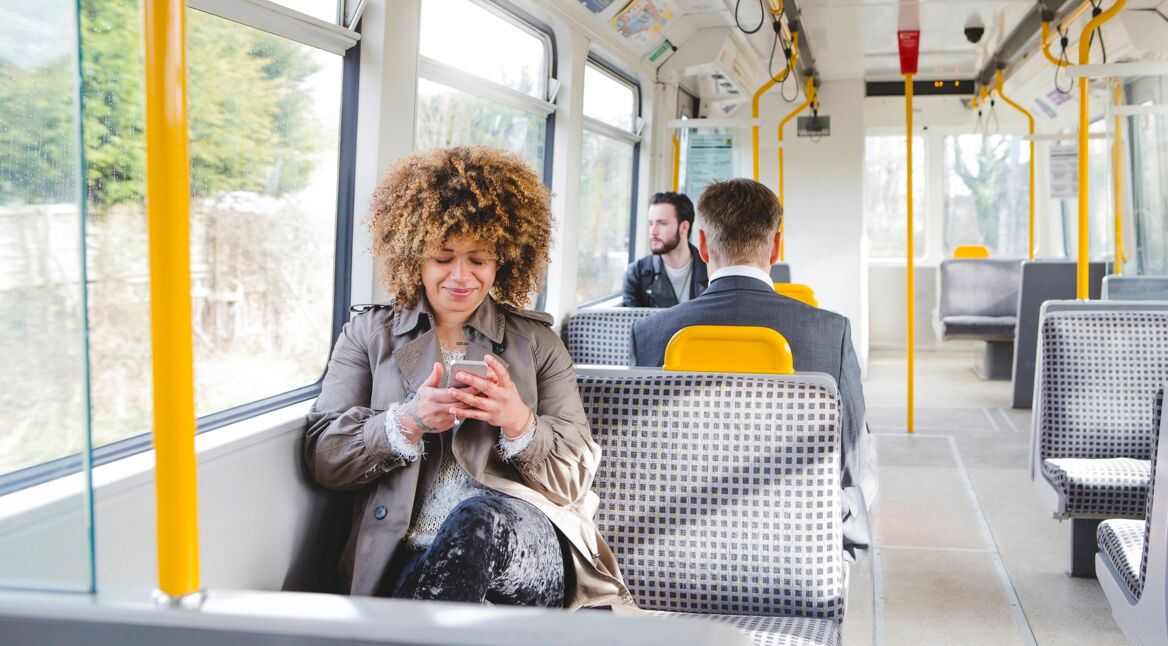 Eine junge Frau sitzt in einem Bus und schaut auf ihr Handy.