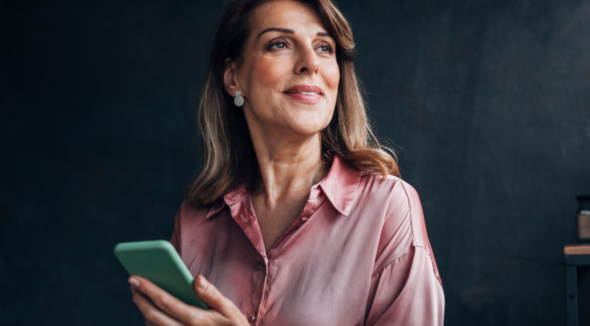 Eine Frau hält ihr Smartphone in der Hand und lächelt