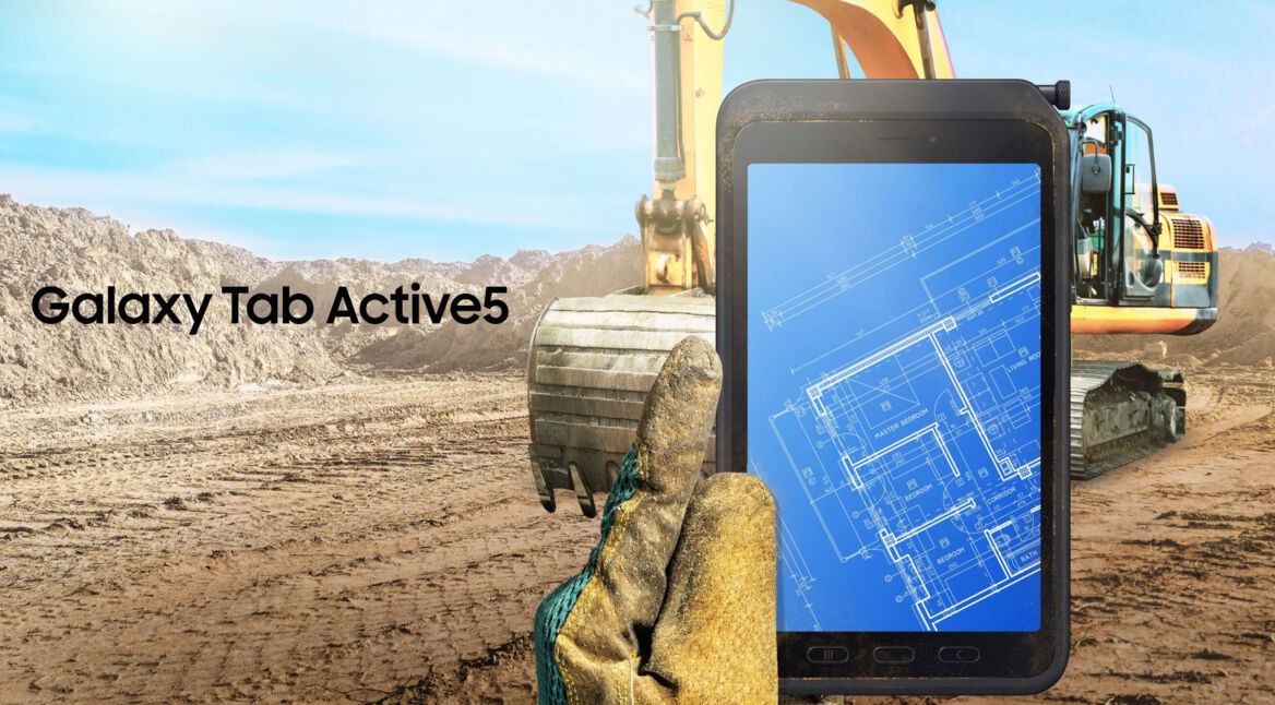 Hand mit Handschuh hält das Tablet Galaxy Tab Active5, im Hintergrund eine Baustelle mit Bagger