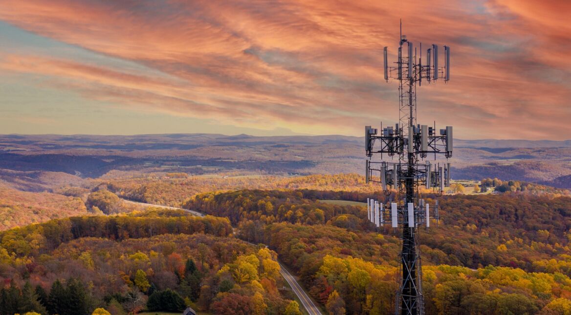 Ein Sendemast in einer ländlichen Gegend, in der eine Straße durch einen Wald führt.