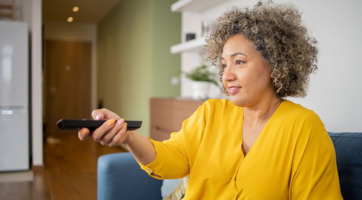 Frau sitzt auf dem Sofa und drückt auf ihre Fernbedienung
