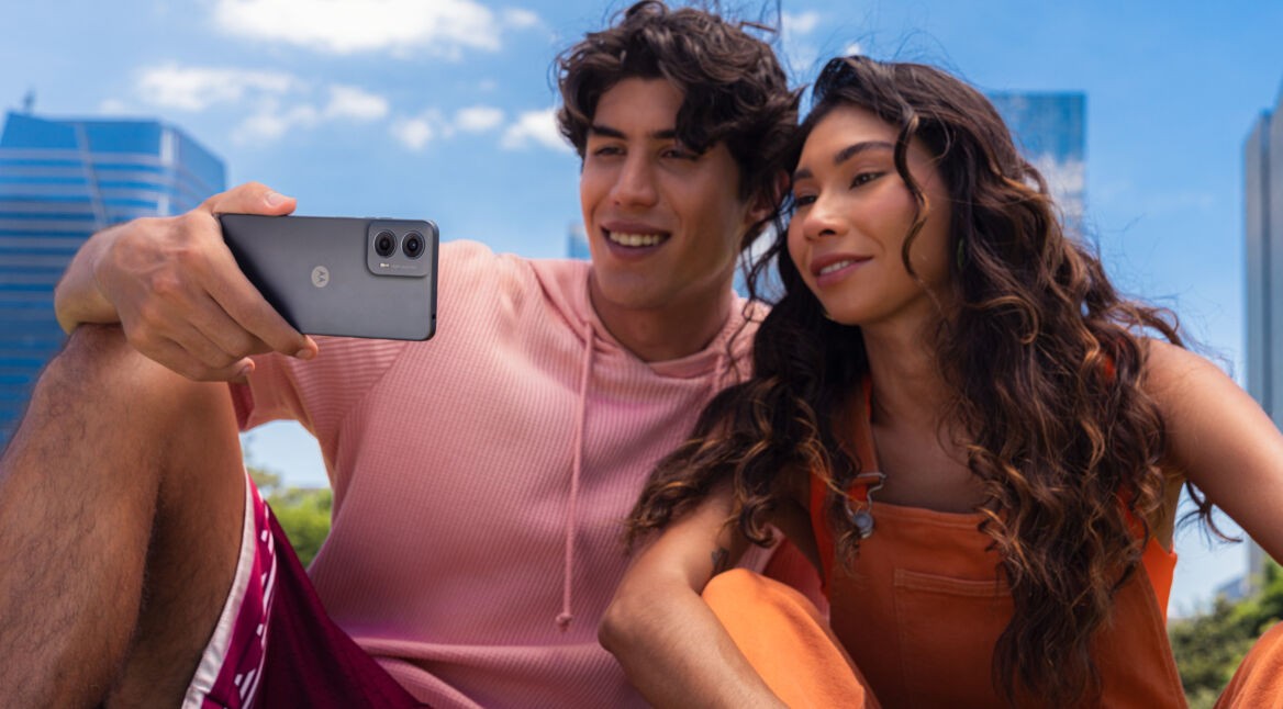 Ein junger Mann und eine junge Frau gucken unter freiem Himmel zusammen auf das Display des Handys Moto G24