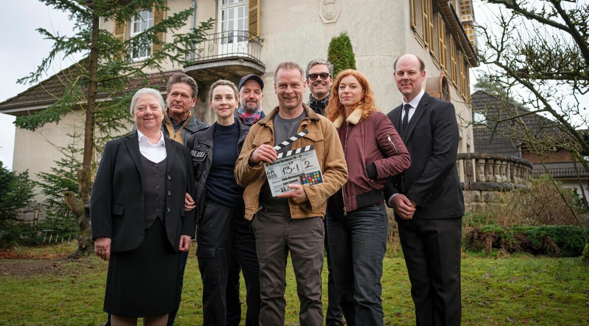 Schauspieler posieren vor DRehbeginn vor einem Haus.