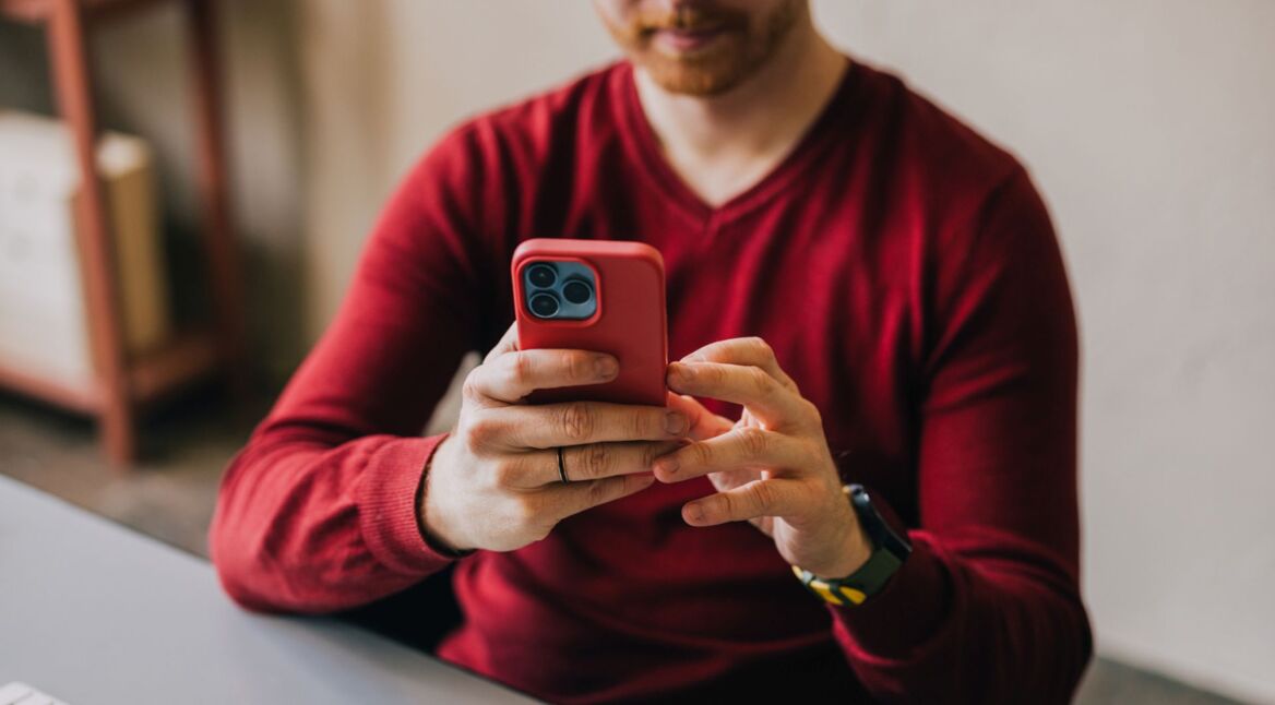 Mann tippt auf seinem roten iPhone