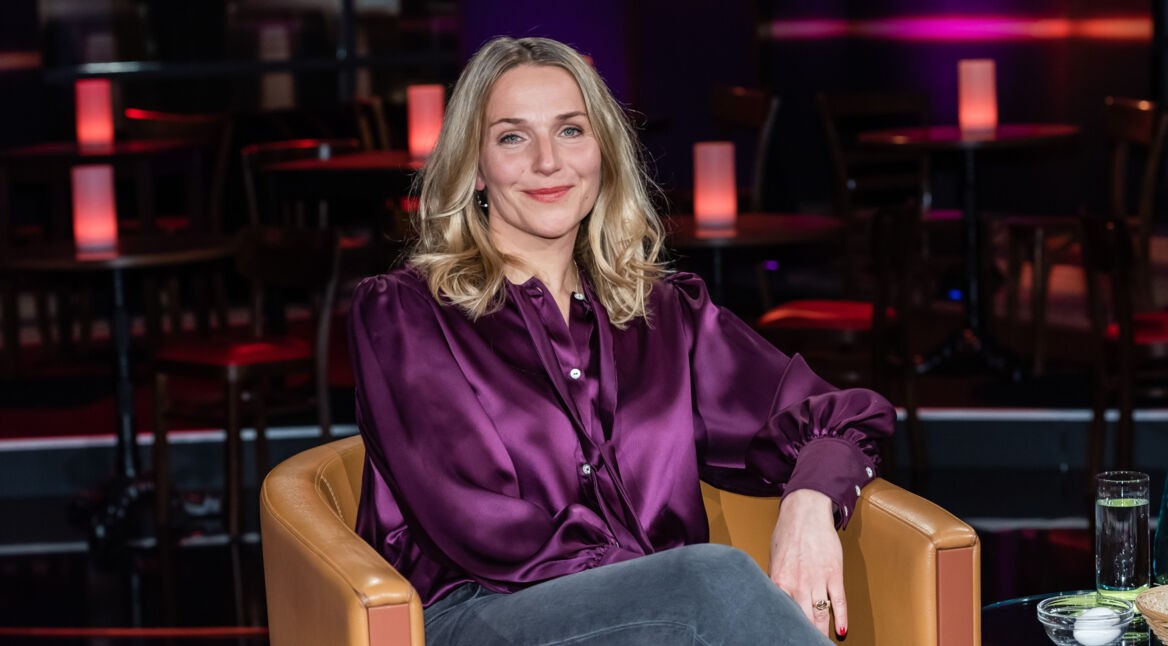 Schauspielerin Tanja Wedhorn sitzt mit lila Bluse auf dem Stuhl eines Fernsehstudios