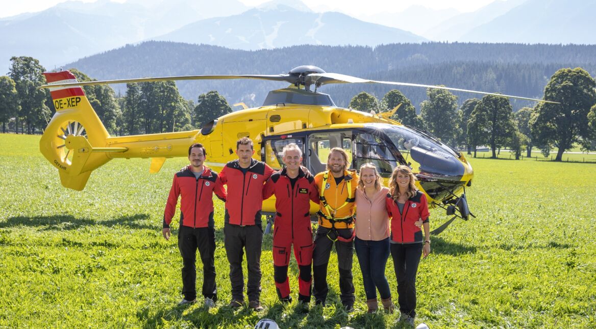 Sechs Personen vor einem Rettungshubschrauber in den Alpen