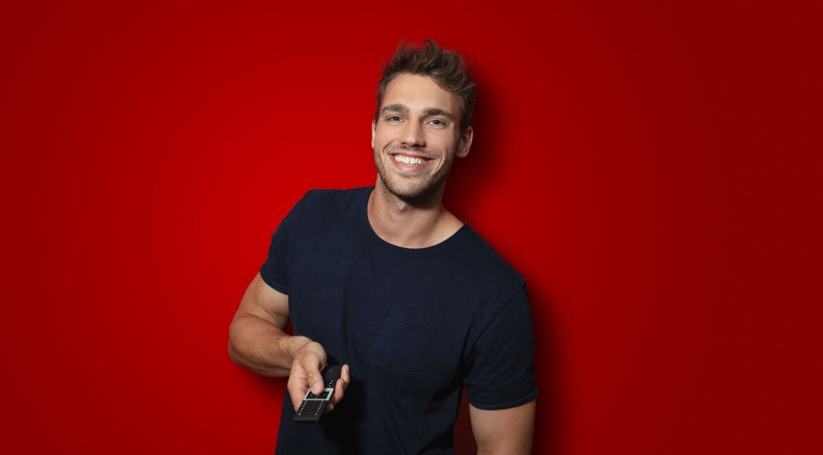 Ein Mann hält eine Tv-Fernbedienung in der Hand und lächelt