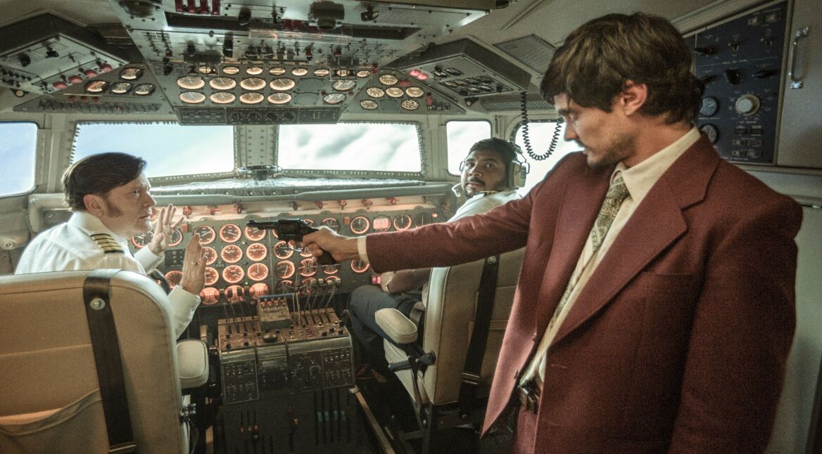 Szenenbild aus der Serie Die Entführung des Flugs 601: Einer der Entführer, wie er mit einer Waffe die beiden Piloten bedroht.